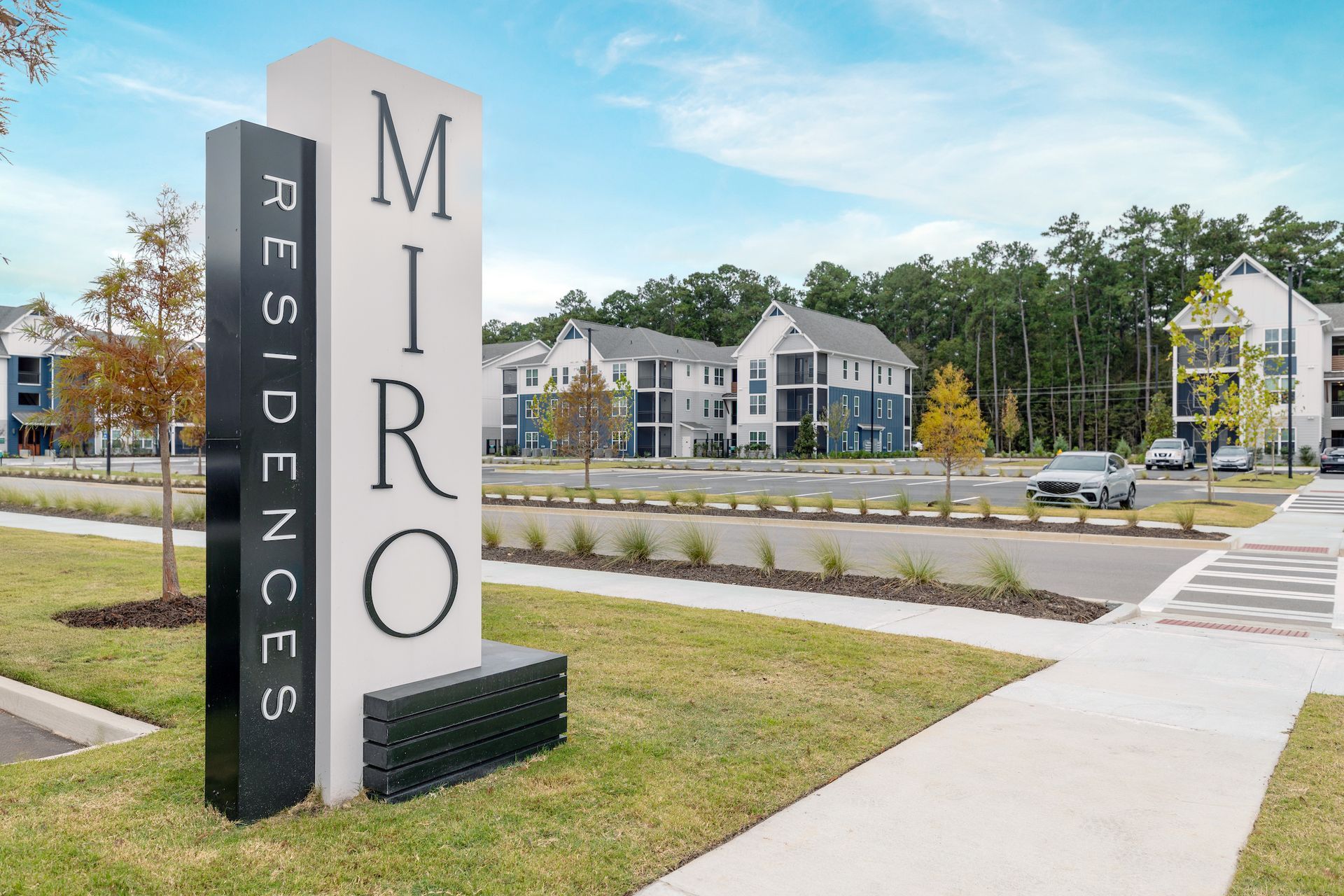 Sign for MIRO RESIDENCES with apartment buildings in the background and a blue sky.