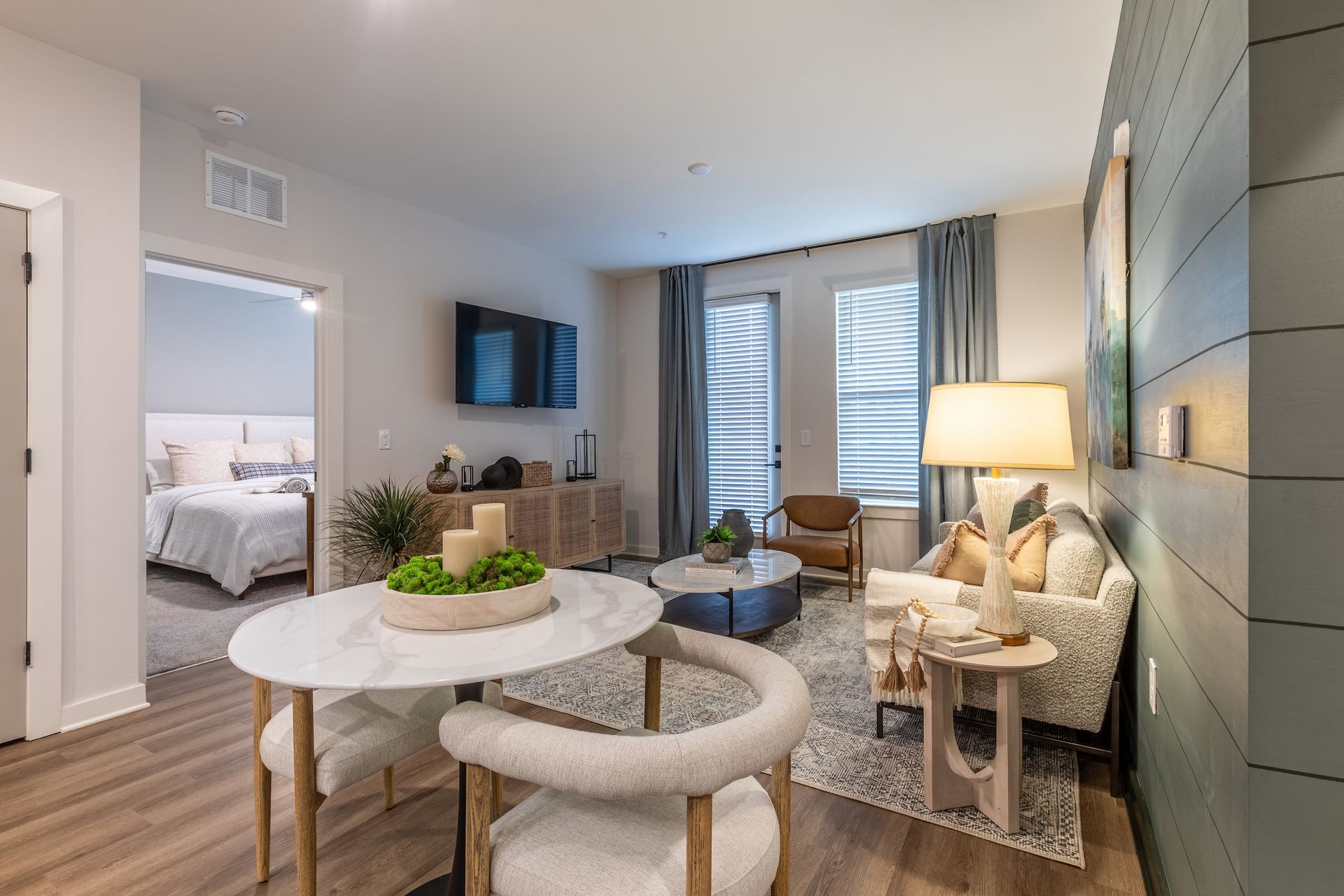Living room with dining table, sofa, TV, and balcony access. Light colors, modern design.