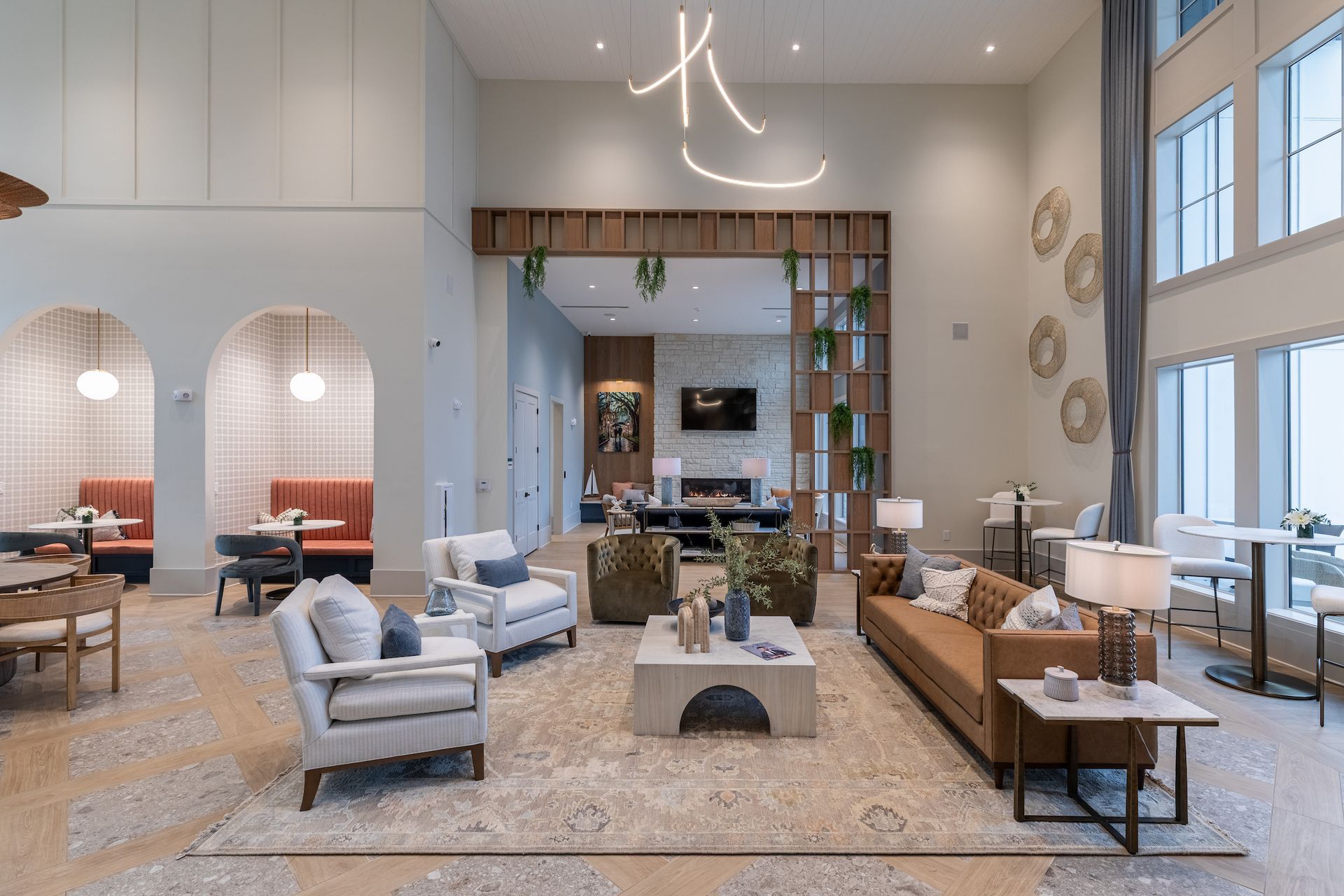 Spacious modern lounge with seating areas, fireplace, and high ceilings, neutral tones, and pendant lighting.