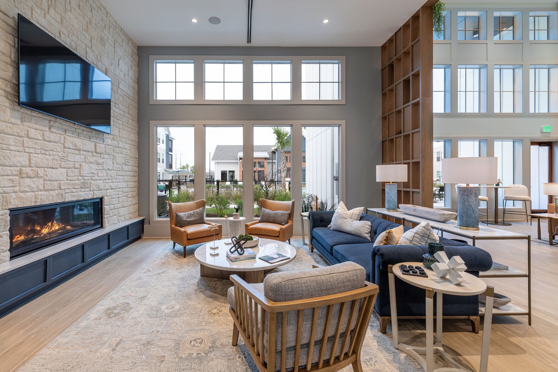 Living room with fireplace, TV, and large windows. Furnished with sofa, chairs, coffee tables, and lamps.
