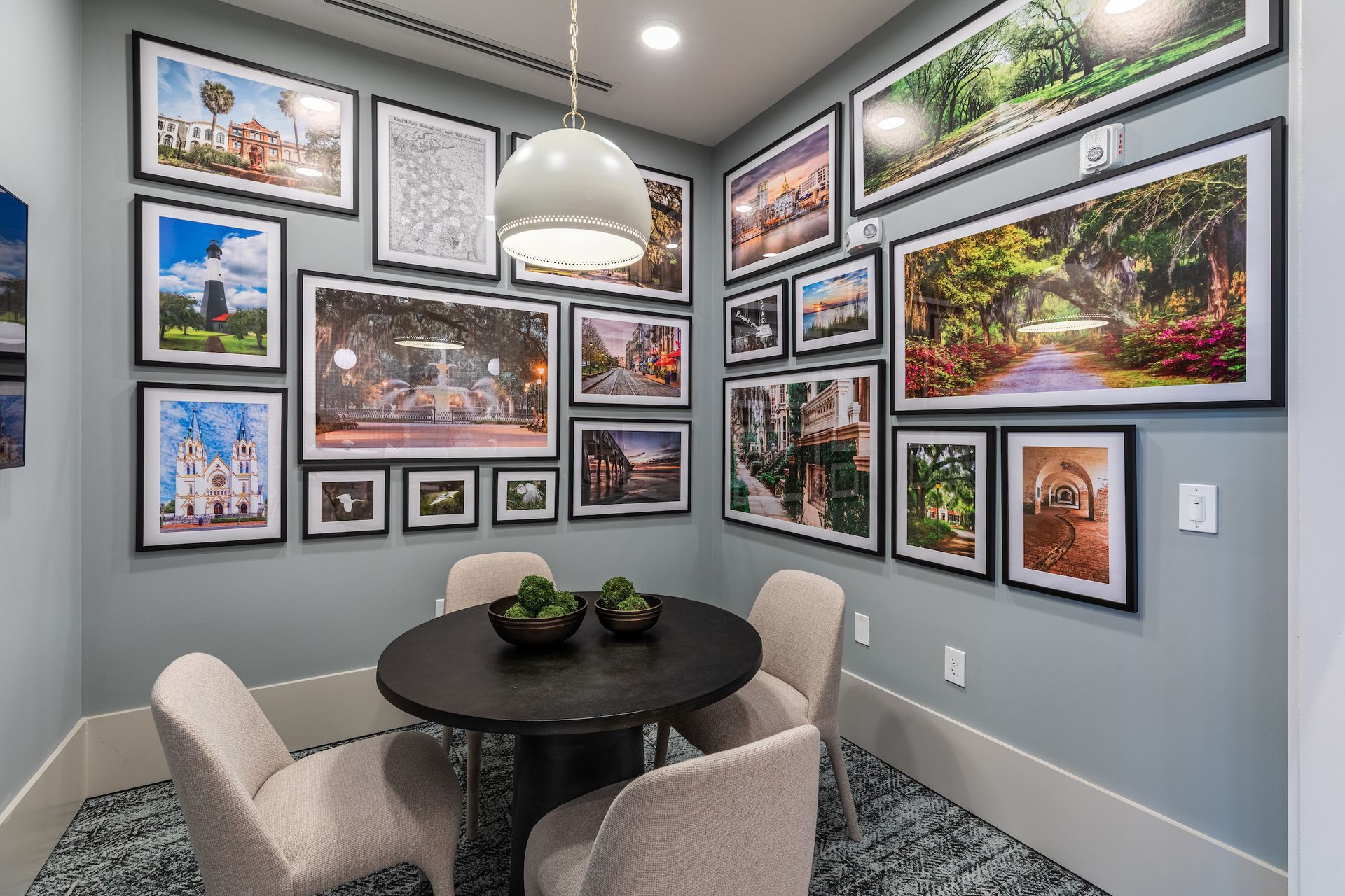 A small dining area with a round black table, four chairs, and framed artwork on the blue walls.