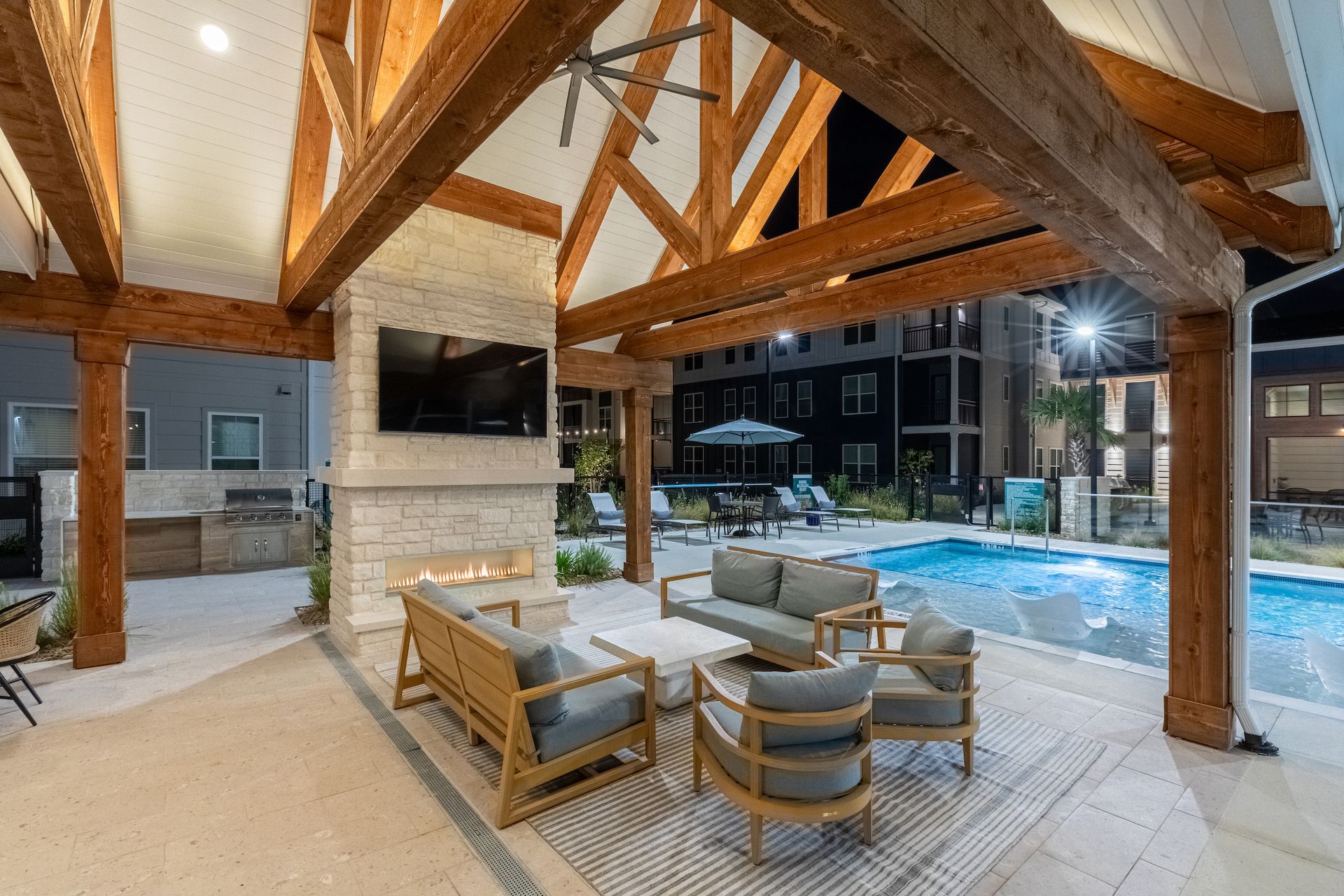 Outdoor lounge area with fireplace, TV, seating, and pool.