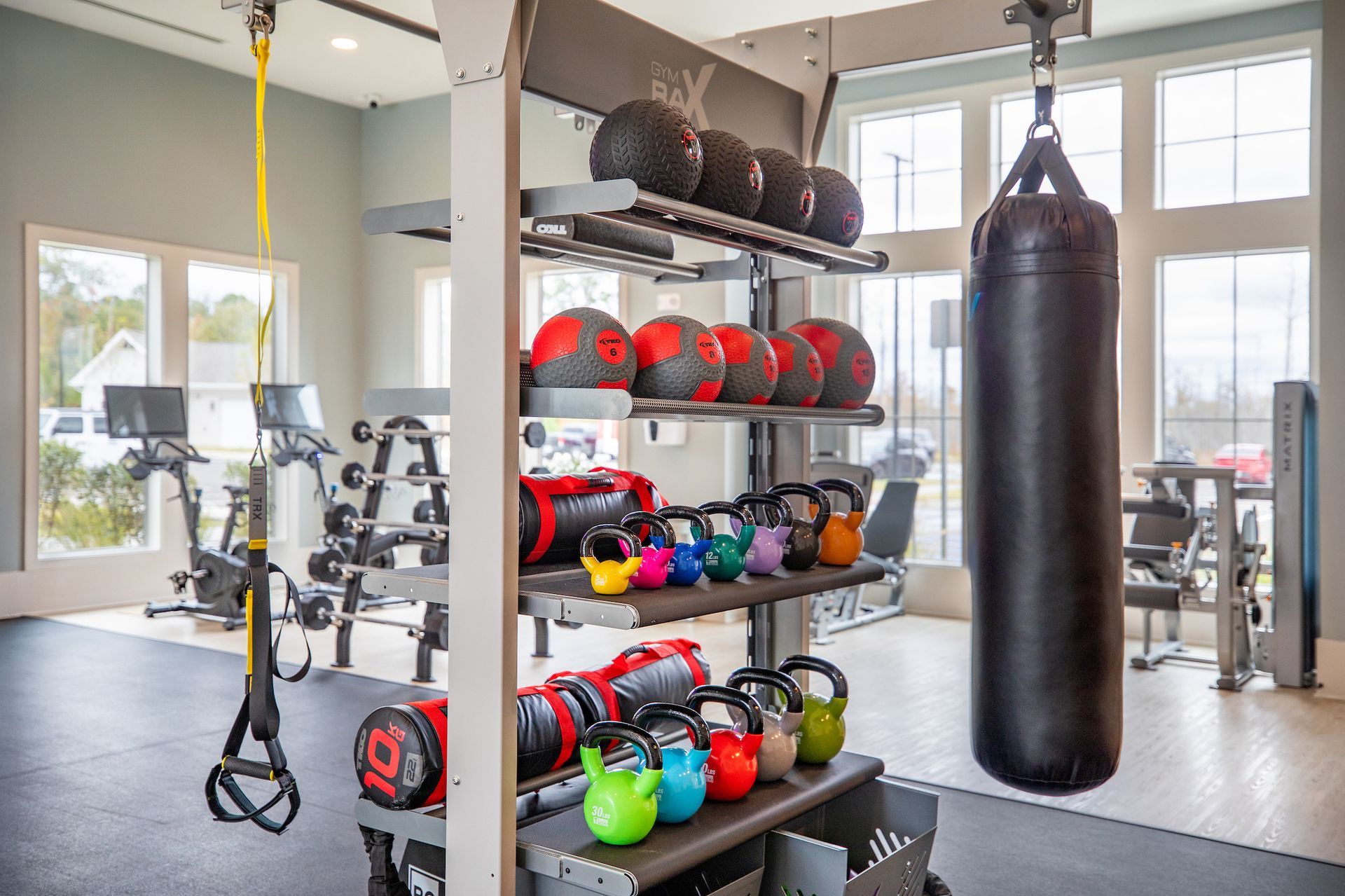 Gym interior with fitness equipment including medicine balls, kettlebells, punching bag, and exercise machines.
