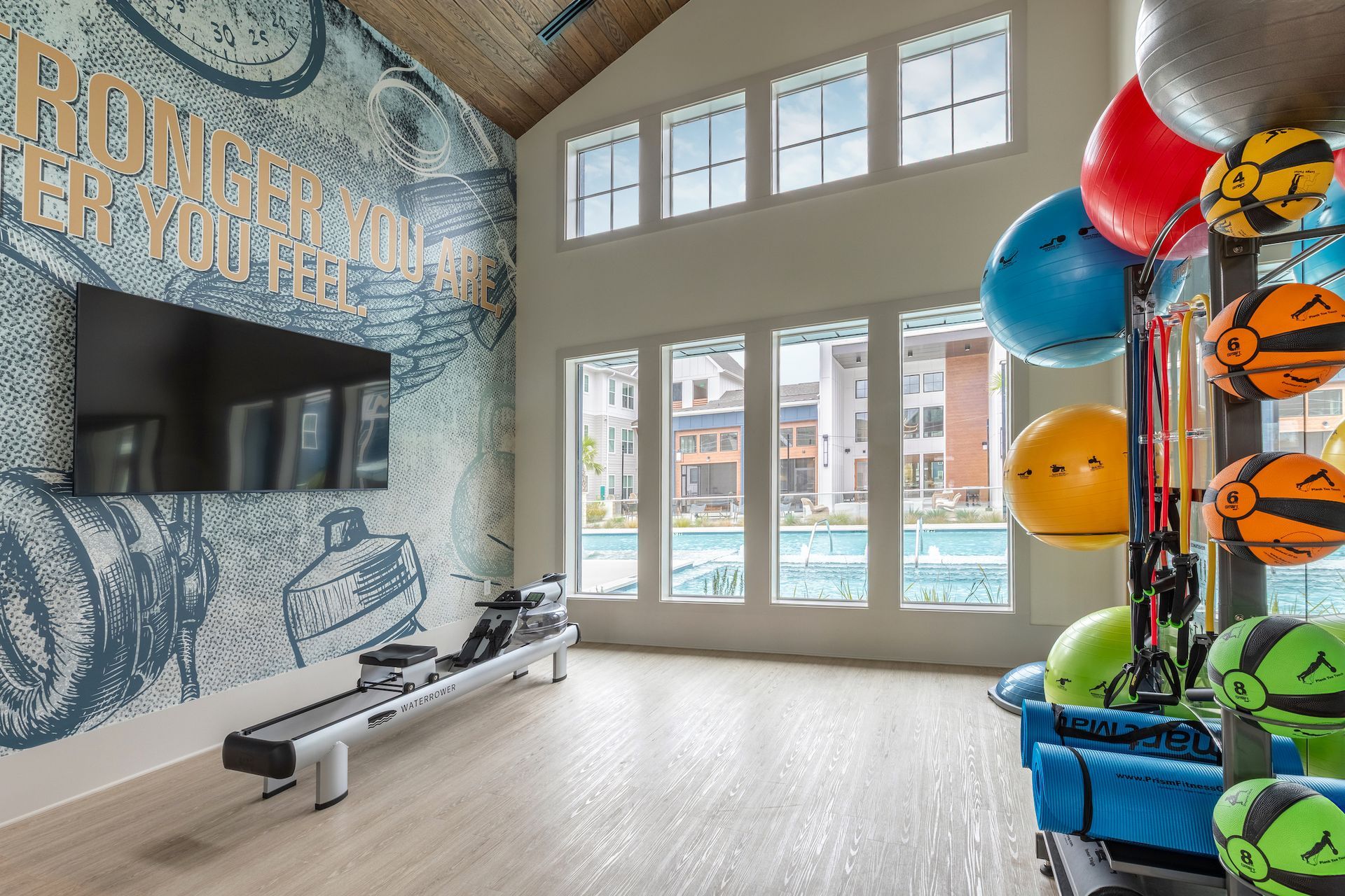 Gym with rowing machine, exercise balls, and view of outdoor pool through windows.