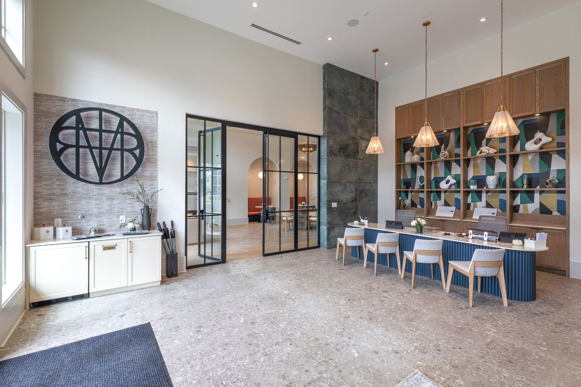 Modern lobby with reception desk, large logo, and glass doors leading to seating area.
