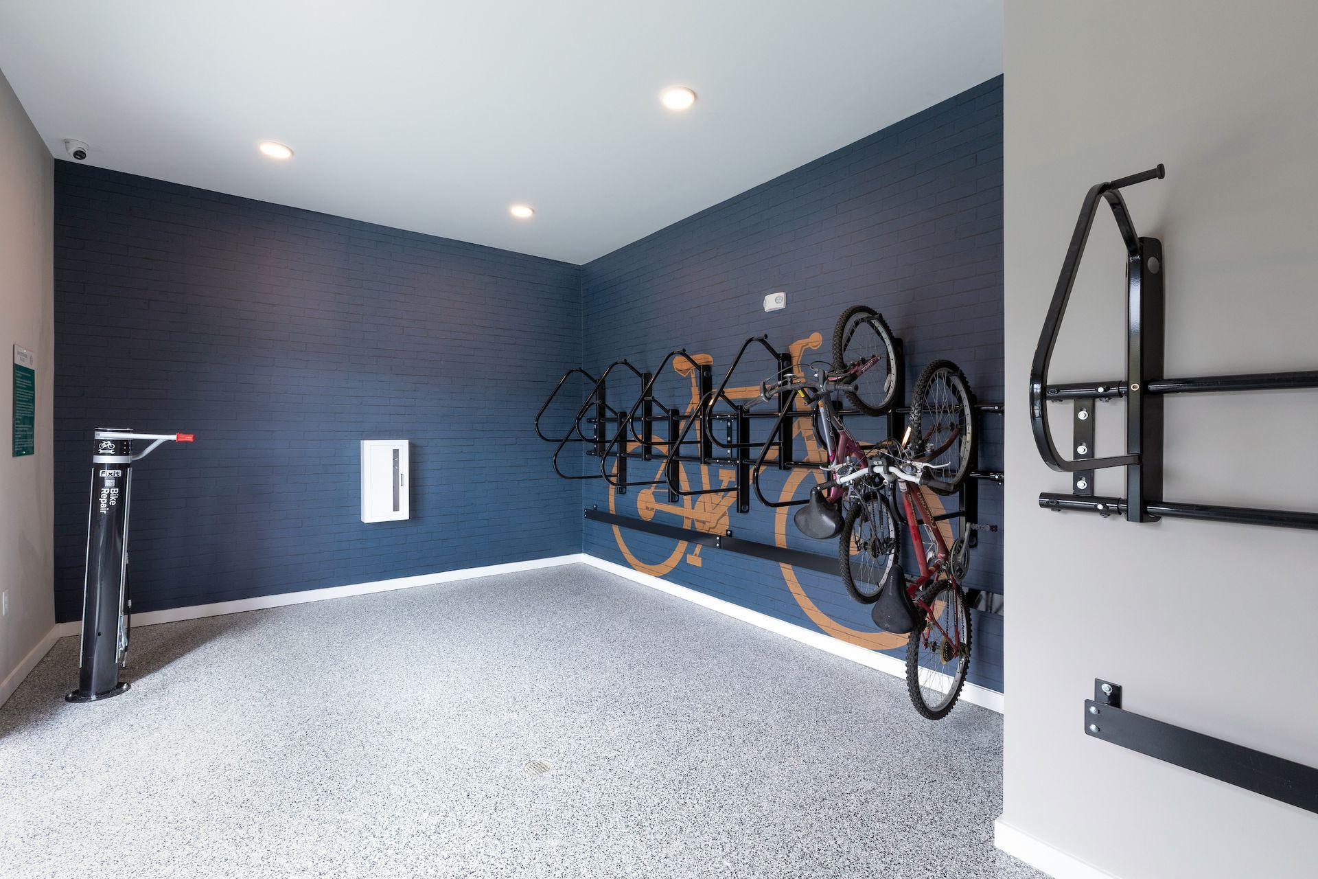 Bike storage room with racks, floor pump, and wall-mounted bike repair stand. Navy and light gray walls.