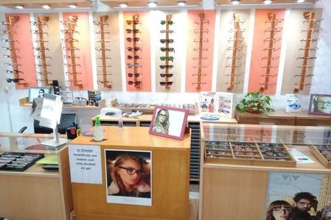 Interior de una óptica con estanterías, mostrador y carteles de gafas enmarcados.