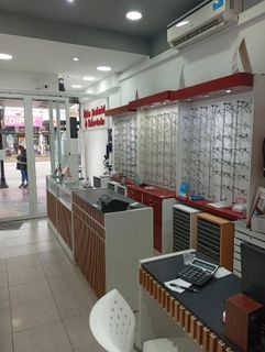 Interior de una óptica con estanterías de exposición, mostradores y una silla blanca cerca de la entrada.