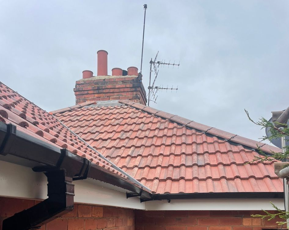 Red-tiled house roof with a brick chimney and TV antenna against a cloudy sky