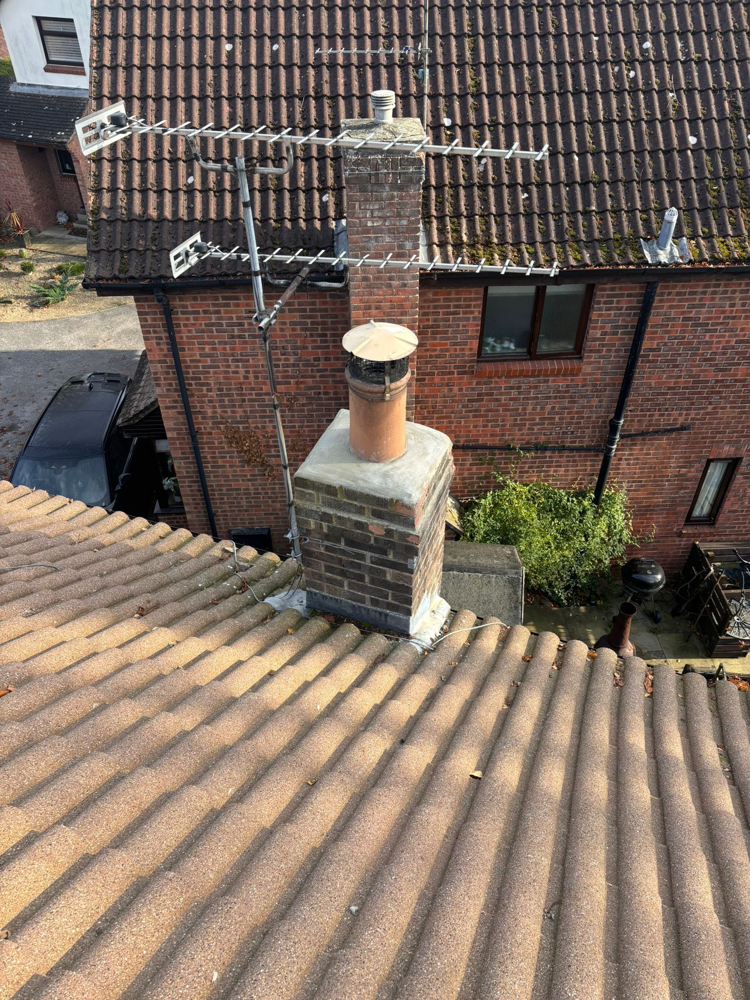 A view from a tiled roof showing a brick chimney stack with a chimney pot and an attached television aerial.