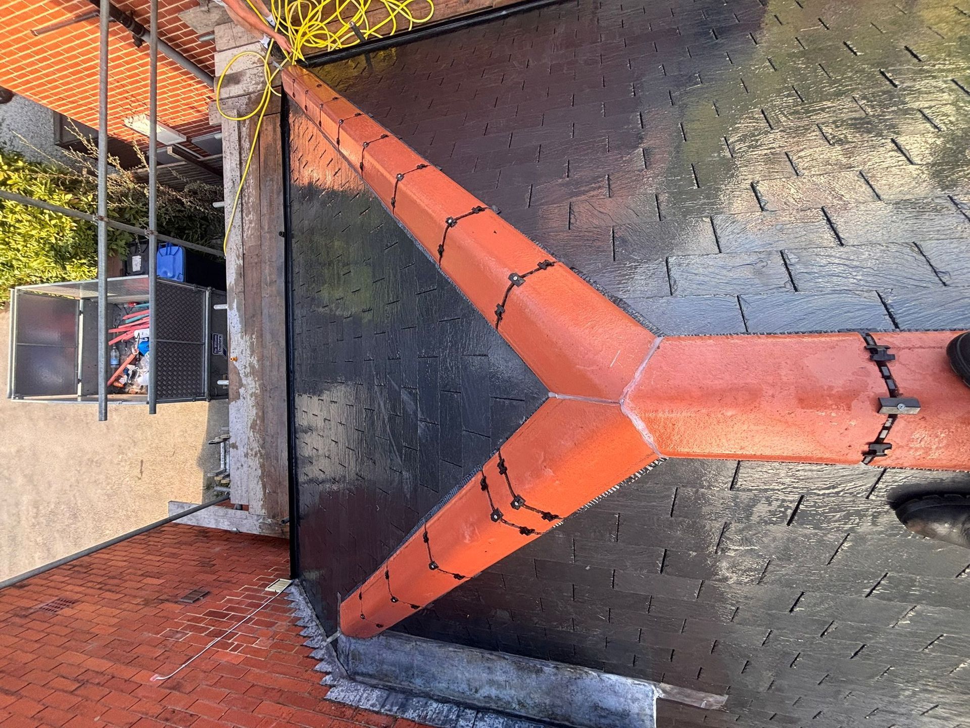 A high-angle view of a newly tiled roof with orange ridge tiles forming a Y-shape over dark gray slate shingles.