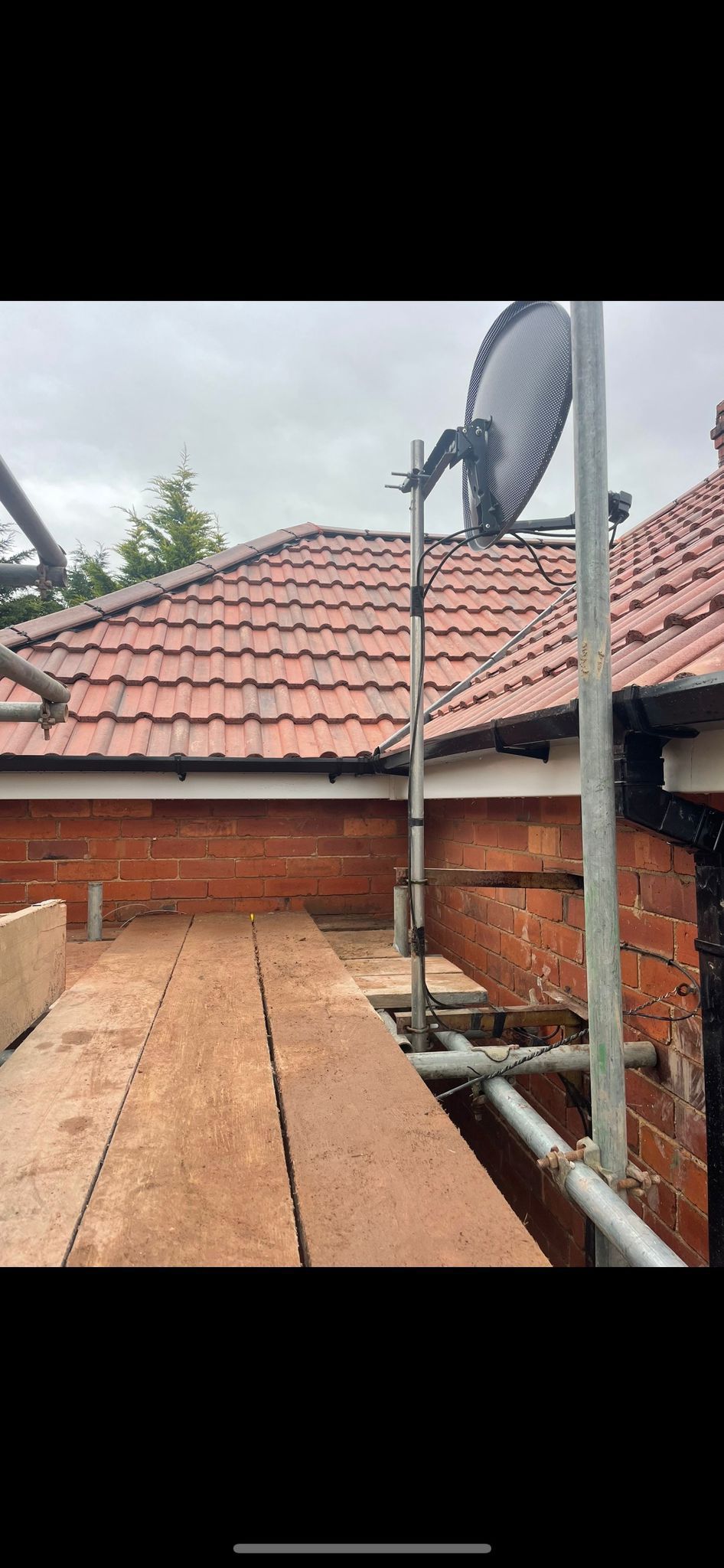 A circular saw blade mounted on a metal pole above scaffolding and a red brick wall on a house roof.
