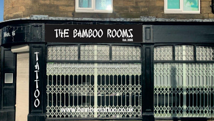The black storefront of The Bamboo Rooms tattoo parlor, showing a sign, vertical tattoo lettering, and security grilles.