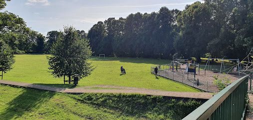 A green park featuring a field, a playground on the right, and trees along the perimeter under a bright sky.