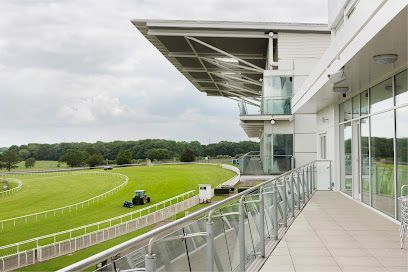 A modern glass balcony overlooking a lush green horse racing track on a cloudy day, with a tractor mowing the grass.