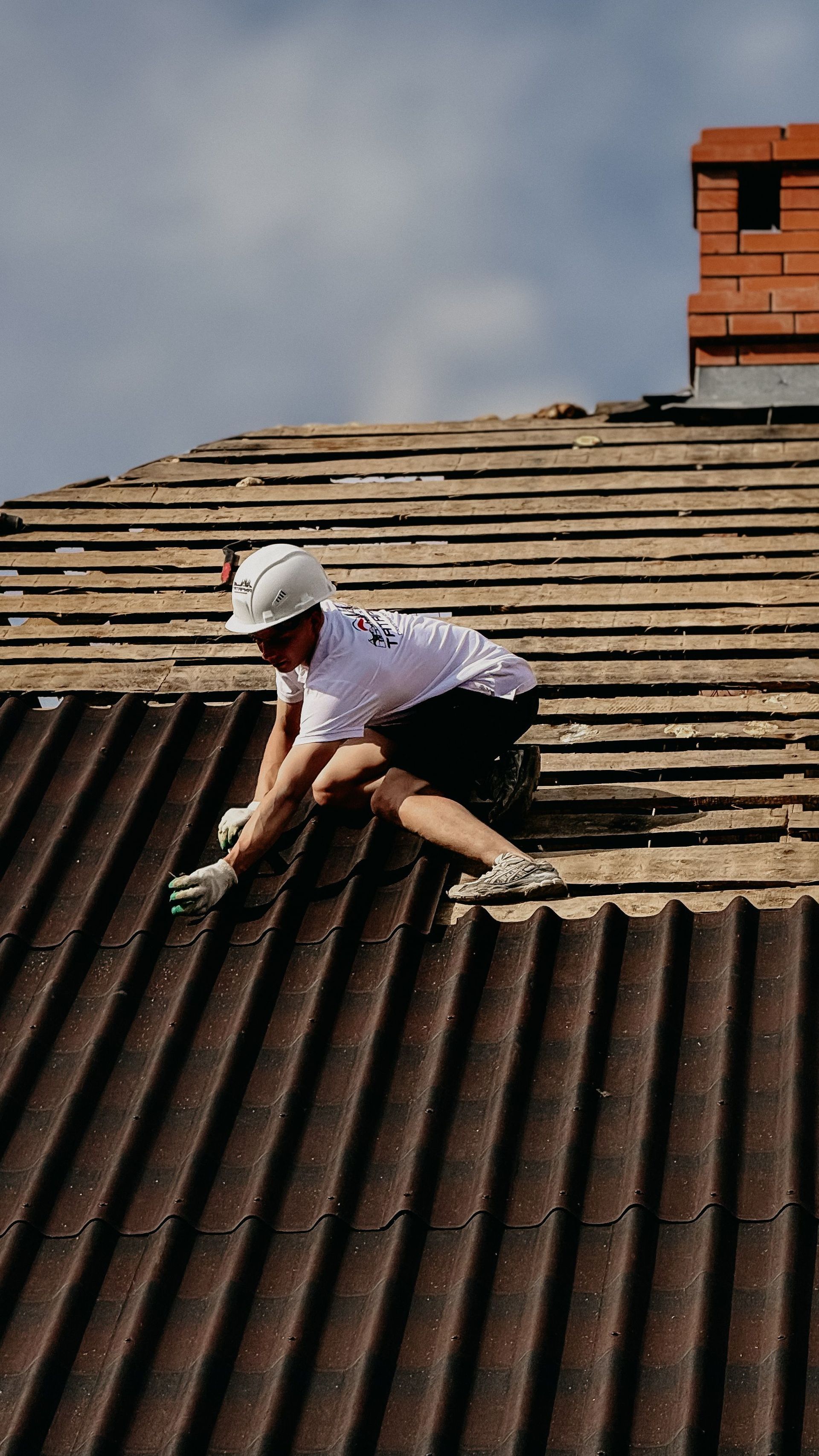 Worker repairing a roof on a tiled house under a cloudy sky