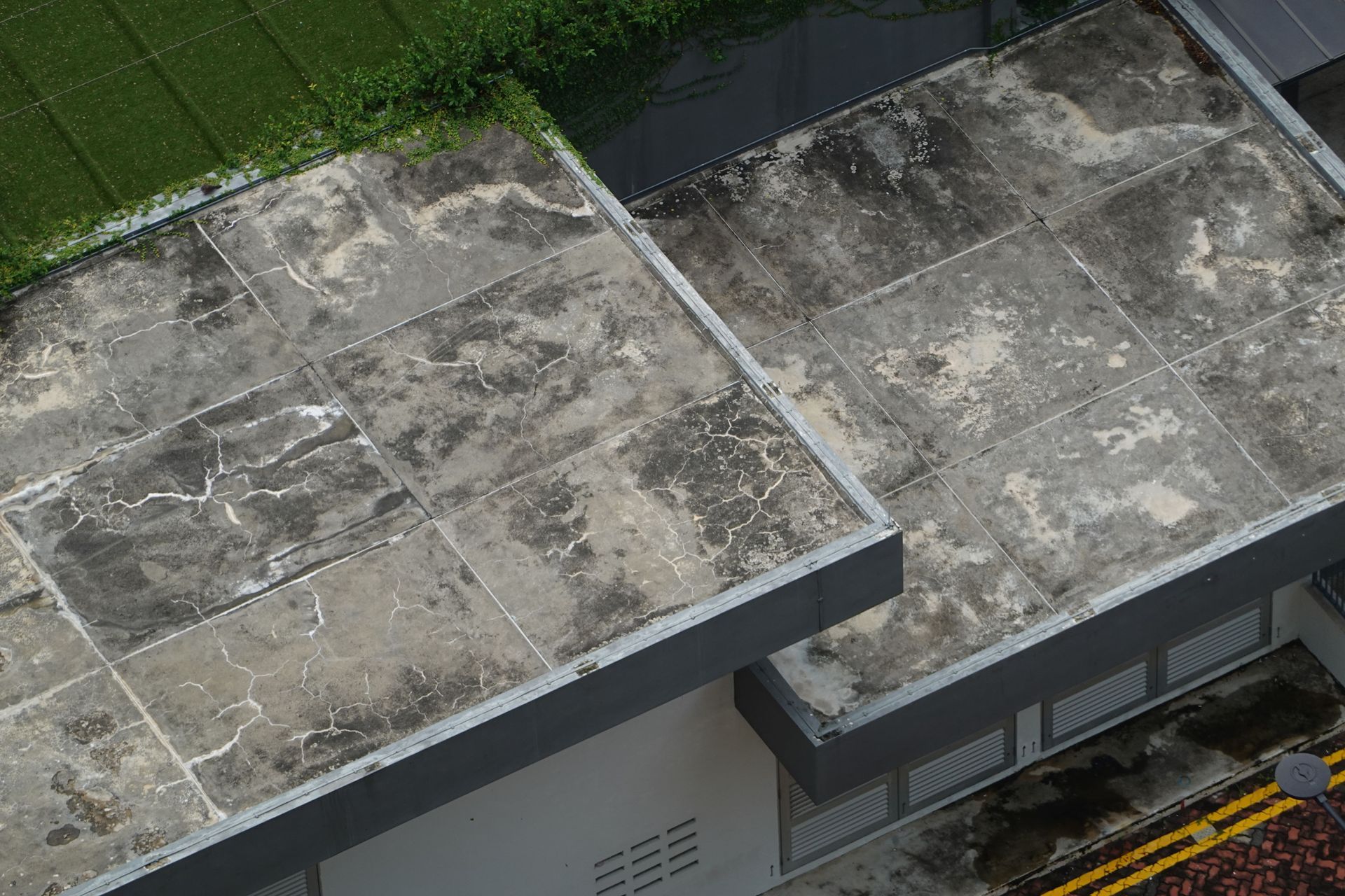 Weathered flat rooftop with gray concrete sections and a strip of green grass at the top edge