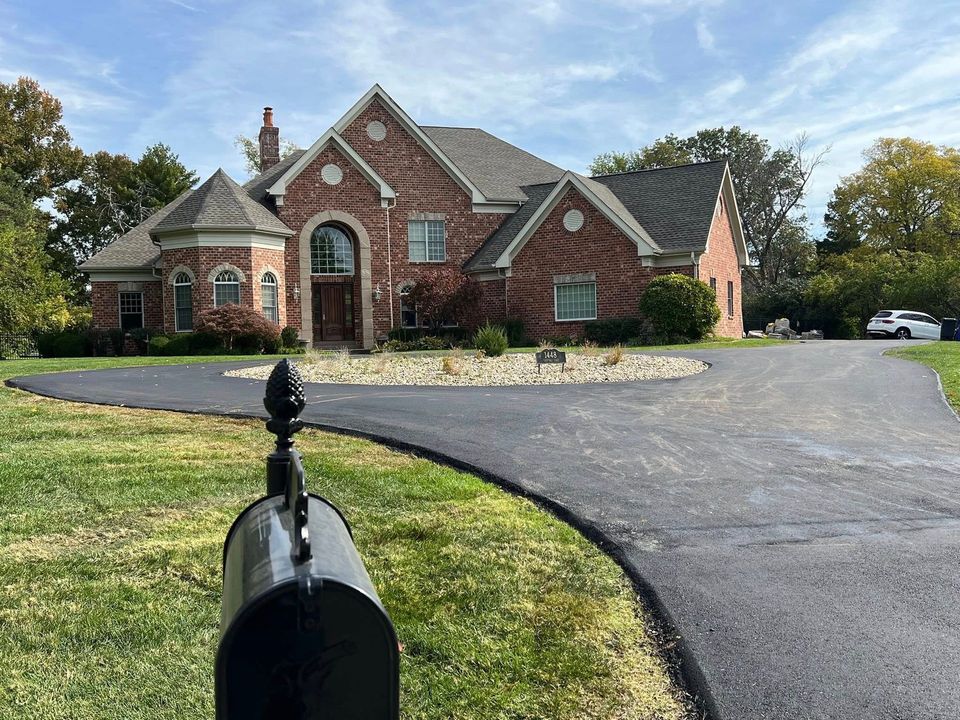 A black mailbox sits in the foreground, with a large, two-story brick house and curved asphalt driveway in the background.