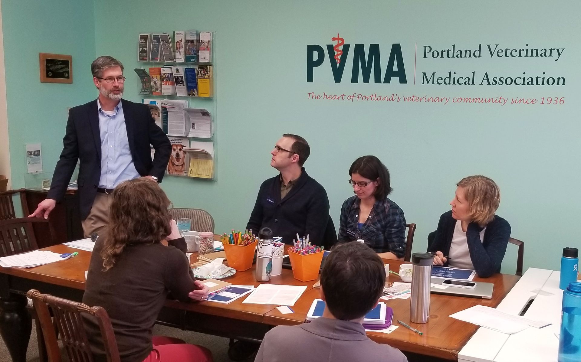 A group of people are sitting around a table in front of a sign that says pvma