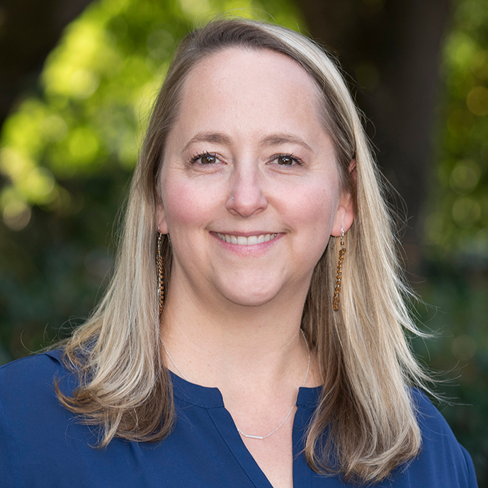 A woman wearing a blue shirt and earrings is smiling for the camera.