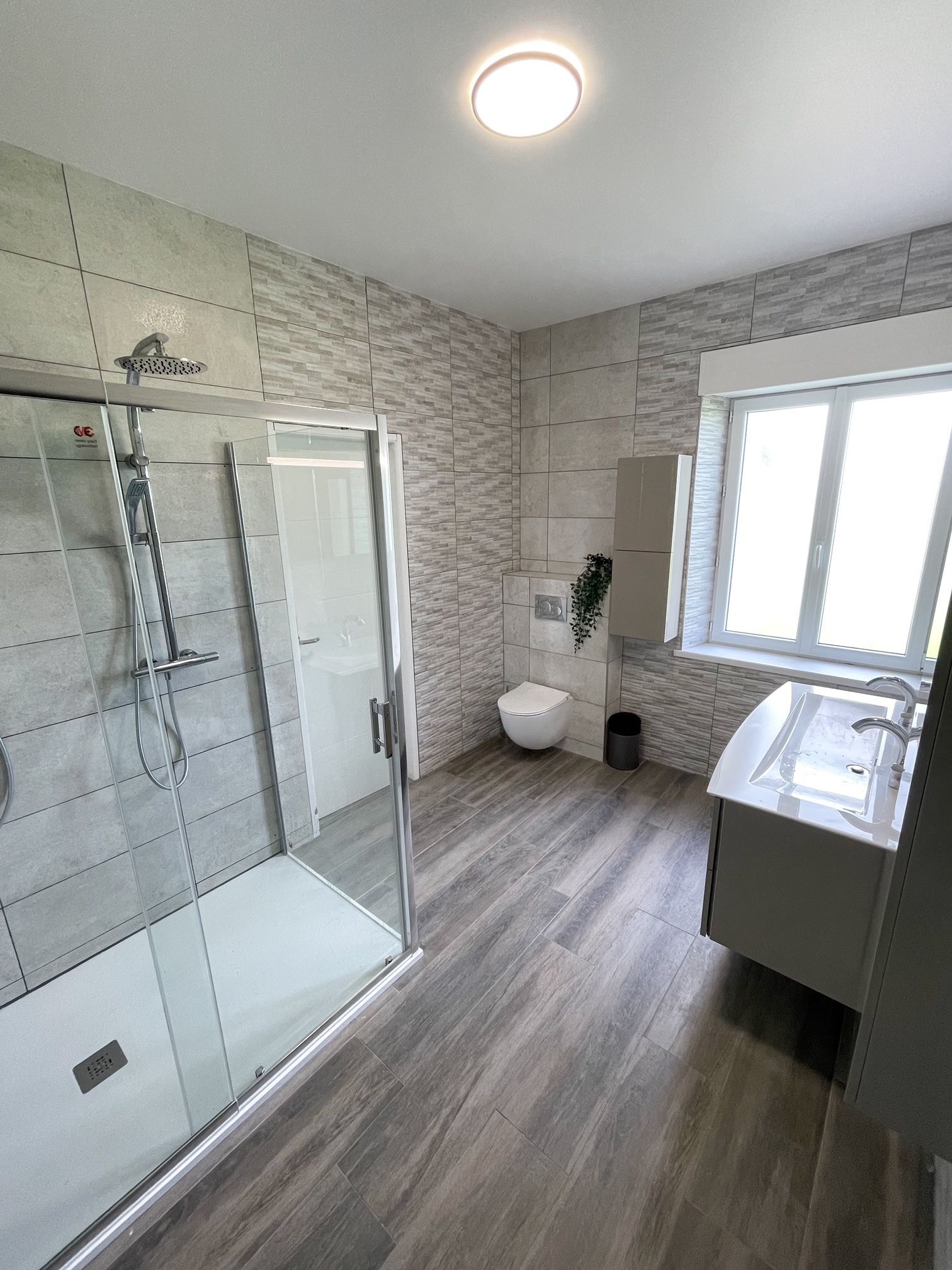 Une salle de bain avec douche à l'italienne, WC, lavabo et fenêtre.