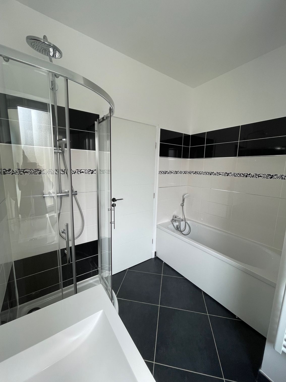 Une salle de bain avec baignoire, lavabo, douche et carrelage noir et blanc.