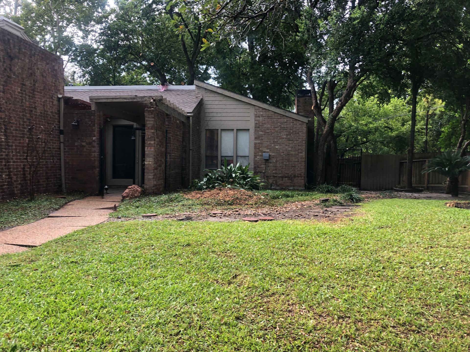 A brick house with a small front yard surrounded by trees; brown brick and a green lawn.