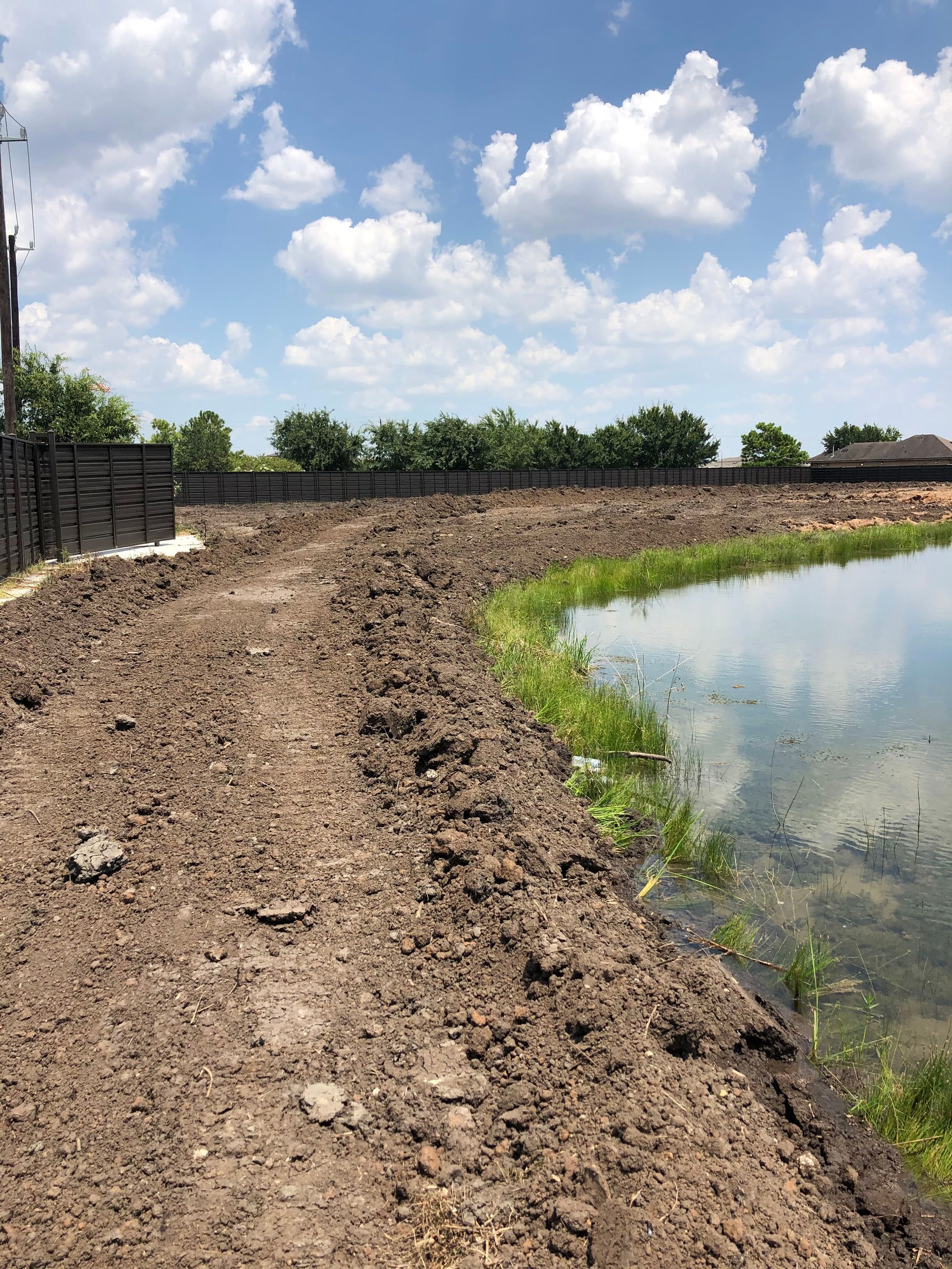 Dirt path next to a pond under a cloudy blue sky.