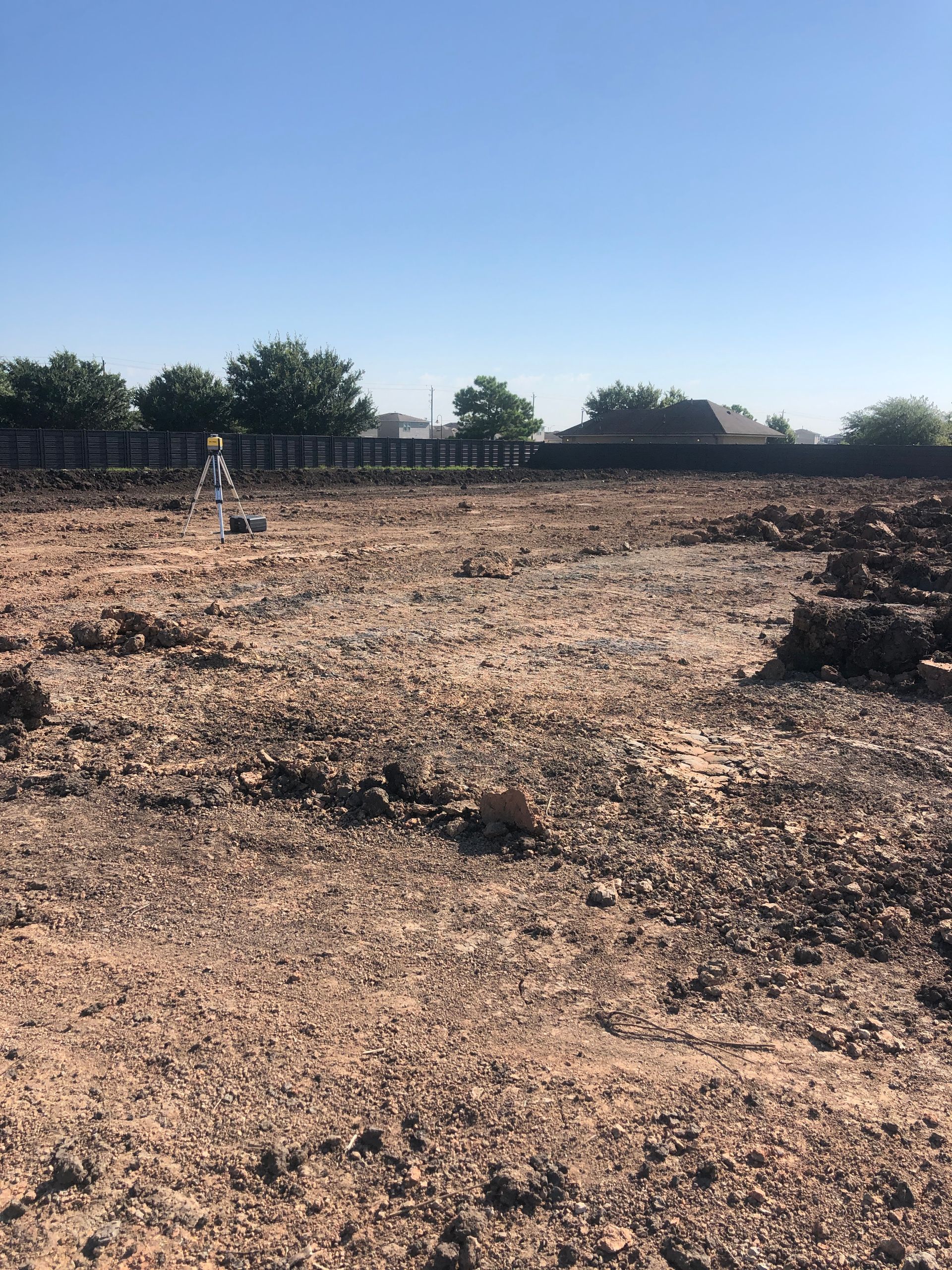 Cleared dirt lot, with surveying equipment in the distance, ready for construction. Sunny day.