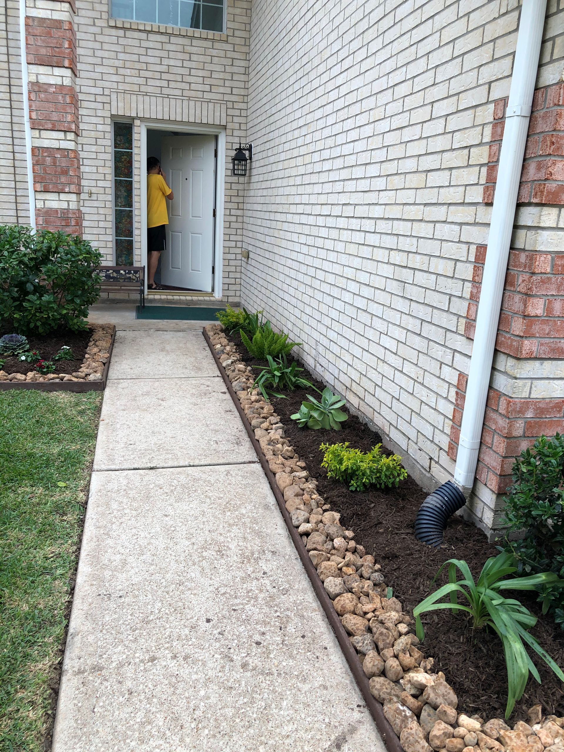 A person in a yellow shirt stands in an open doorway. A concrete walkway leads to the door.