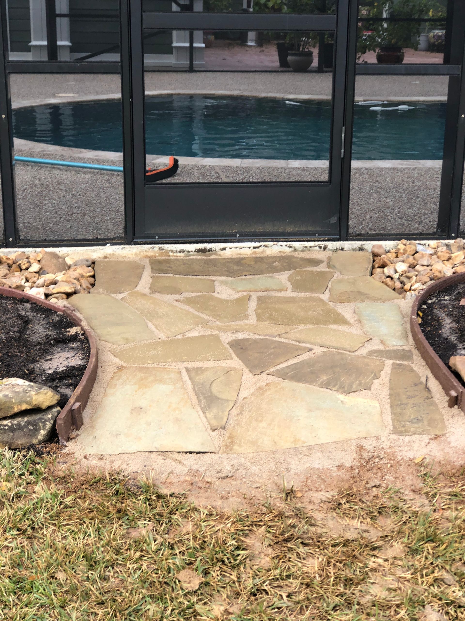 Flagstone pathway leading to a pool enclosure door; the pathway is bordered by flower beds.