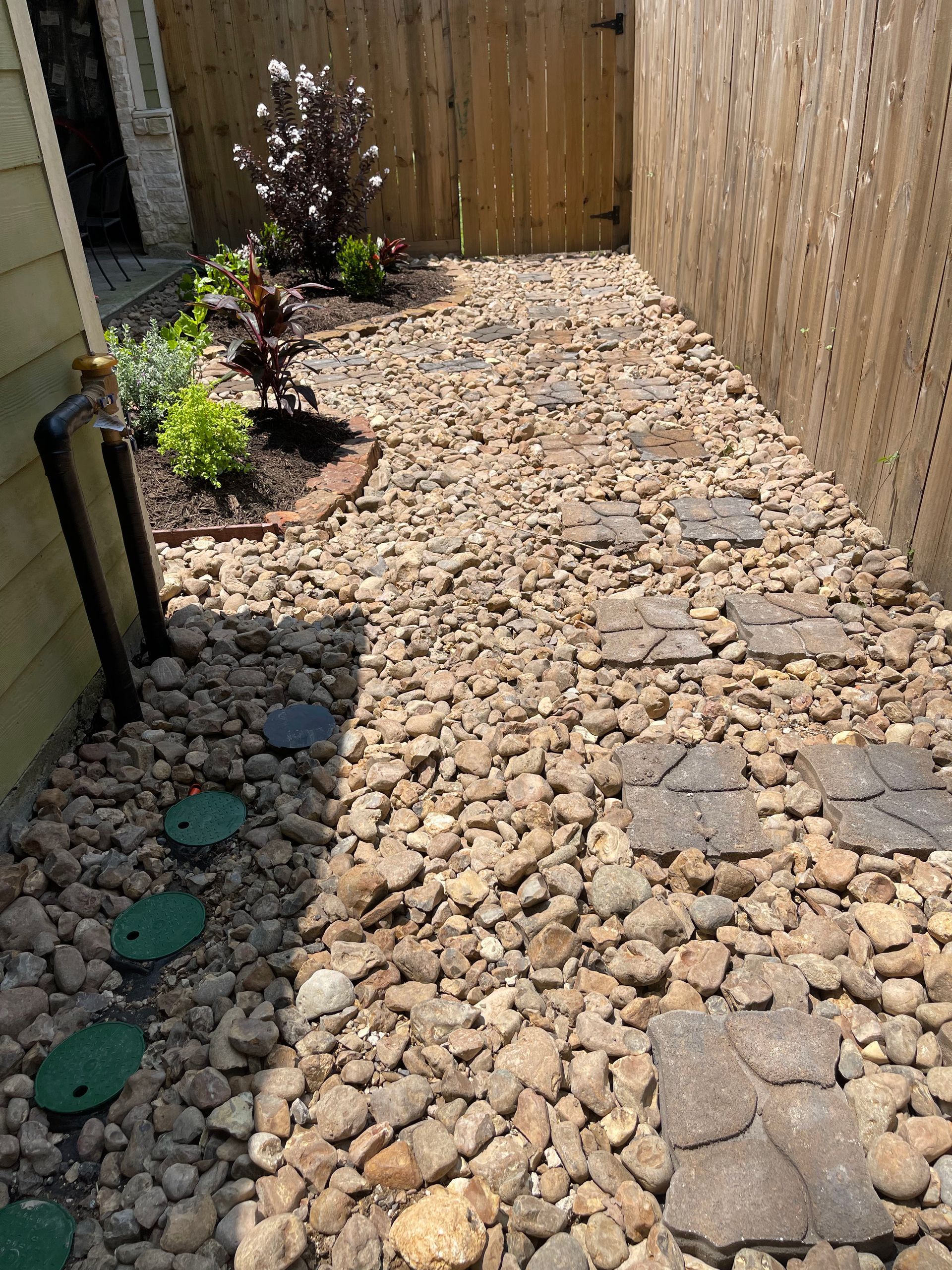 Gravel path with stepping stones between wooden fences and a garden bed with plants.