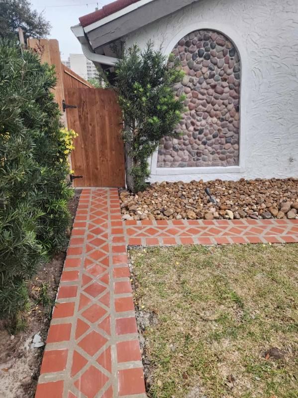 Brick path leading to a wooden gate and house entrance with stone wall detail.