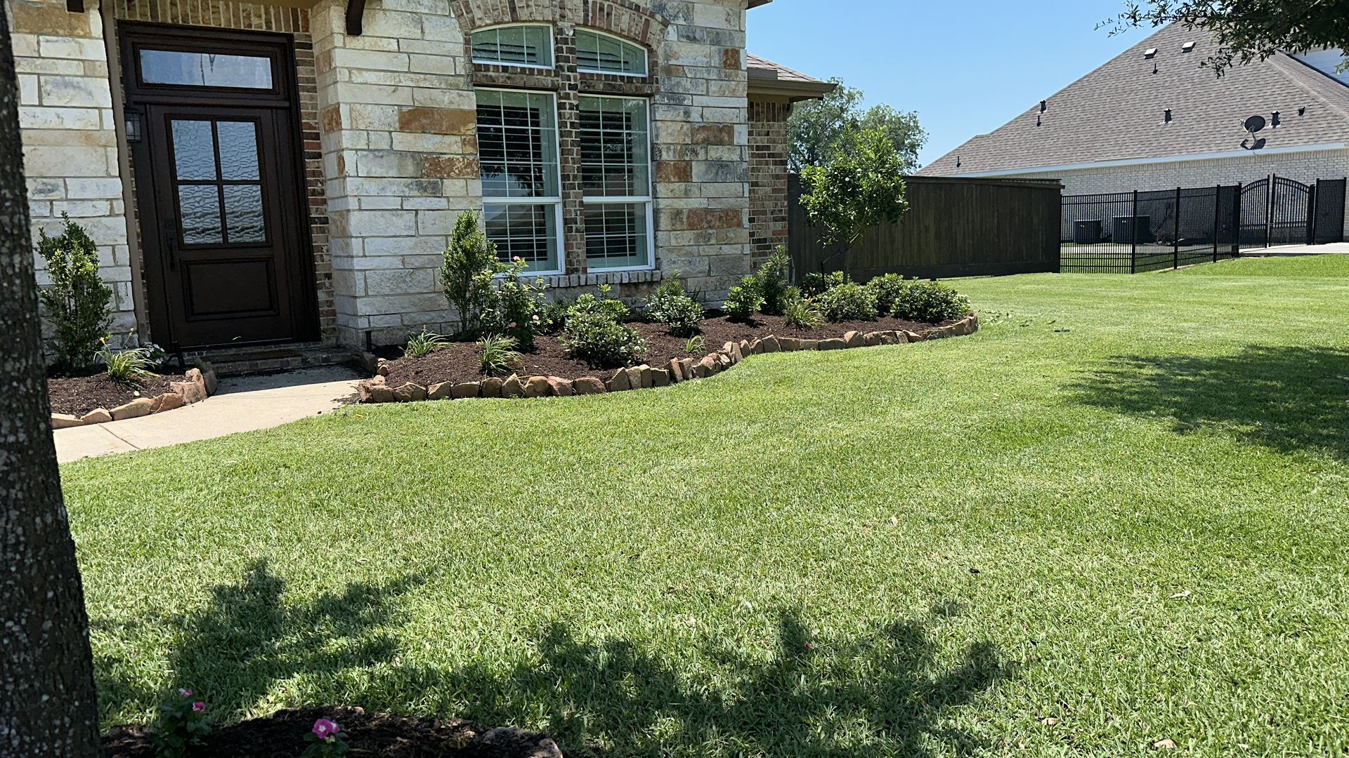 Stone house with brown door, landscaped yard, and green grass.