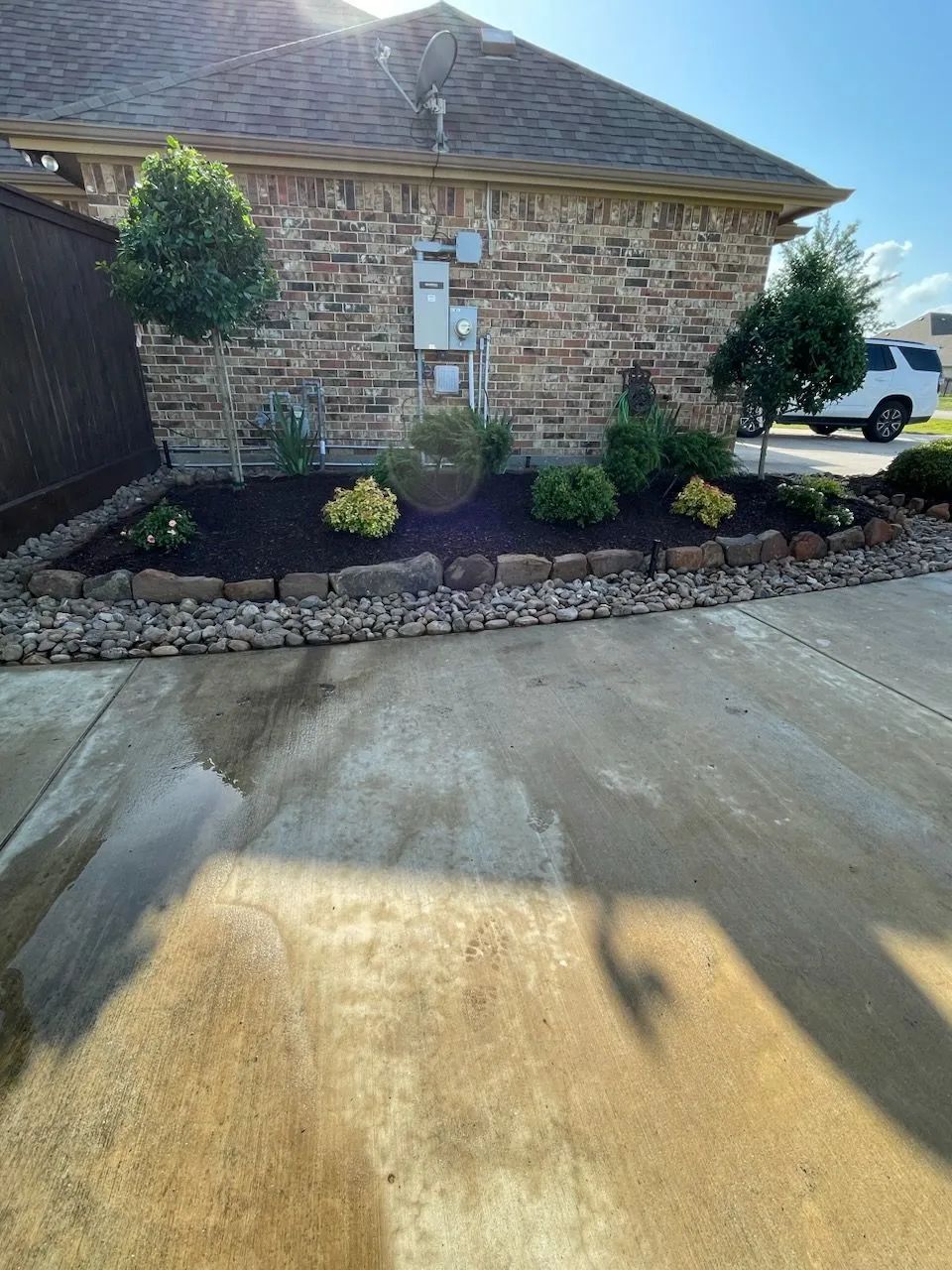 Landscaped garden bed with mulch and shrubs along a brick house; sunny day.