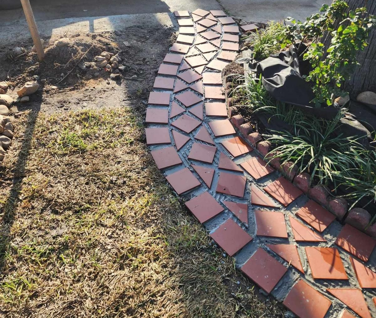 Brick pathway curves through a grassy area, bordering a garden bed.