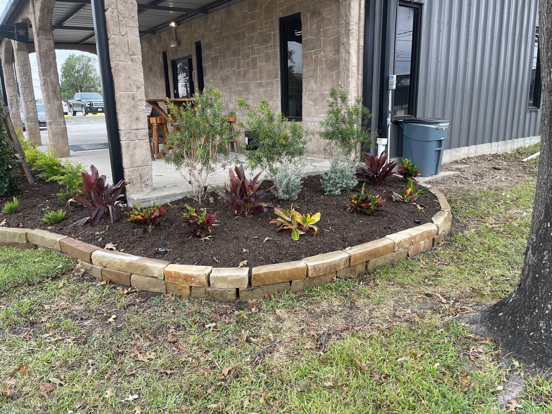 Flower bed with colorful plants bordered by stone blocks next to a building.