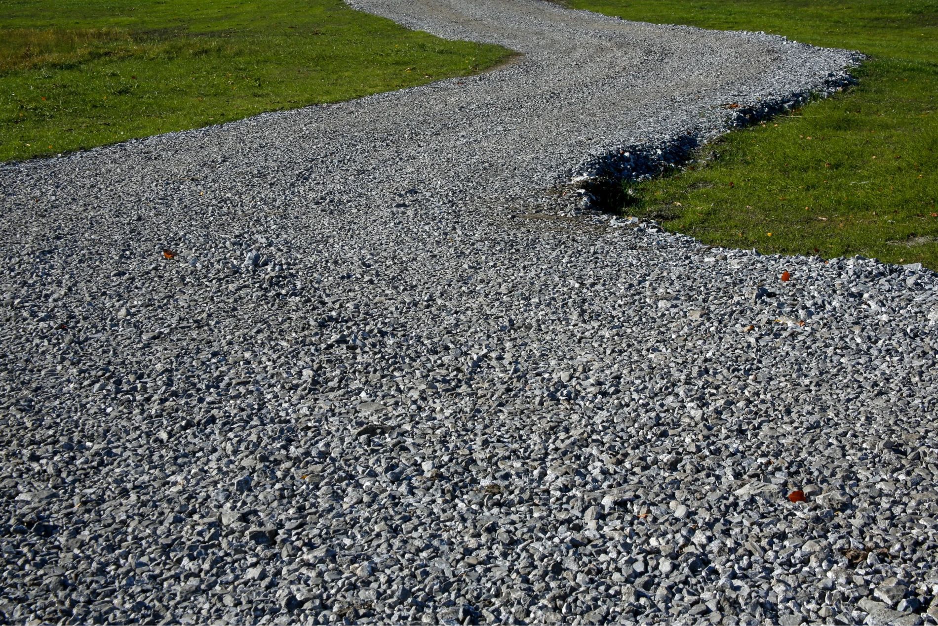 Gravel pathway curves through green grass in an outdoor setting.