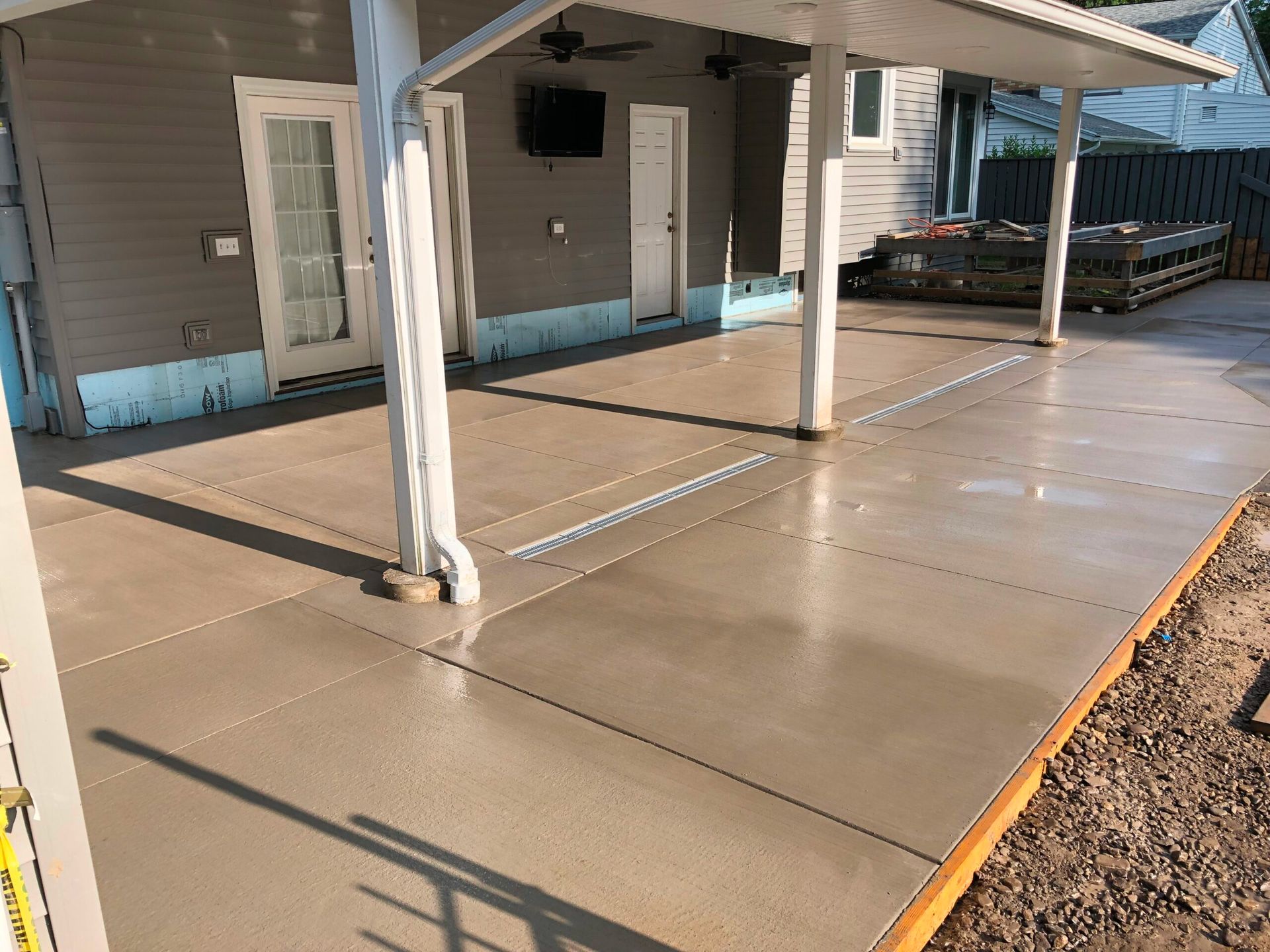 Newly poured concrete patio under a white-columned awning, next to a gray house.
