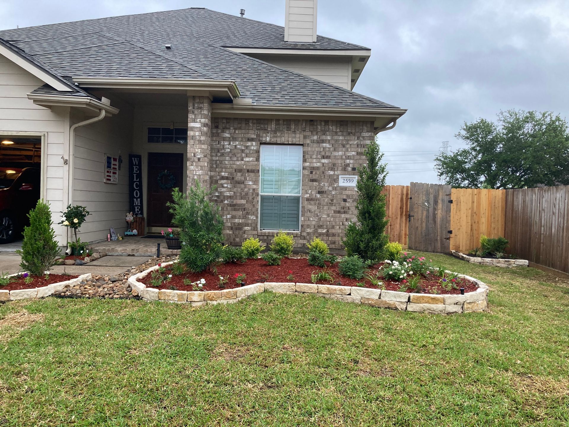 House exterior with landscaped flowerbeds outlined by stone, with green grass and cloudy sky.