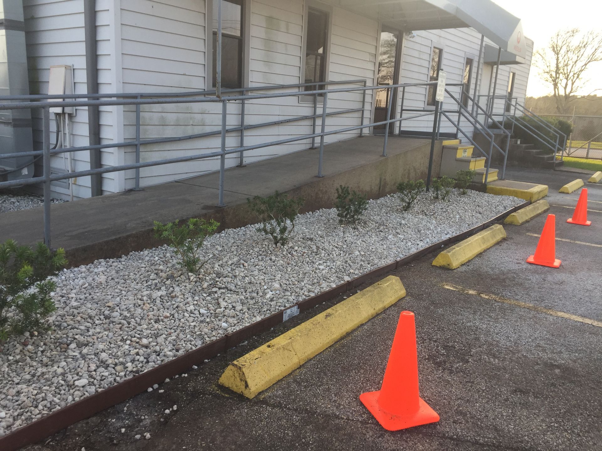 Exterior view of building with accessible ramp, landscaping, parking, and orange cones.