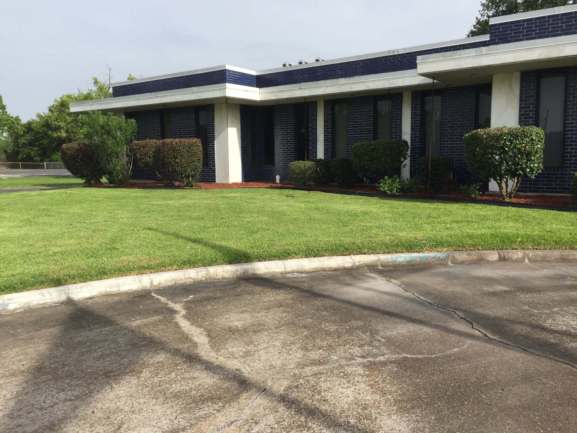 Exterior of a low, blue and white building with green grass and shrubs in front.