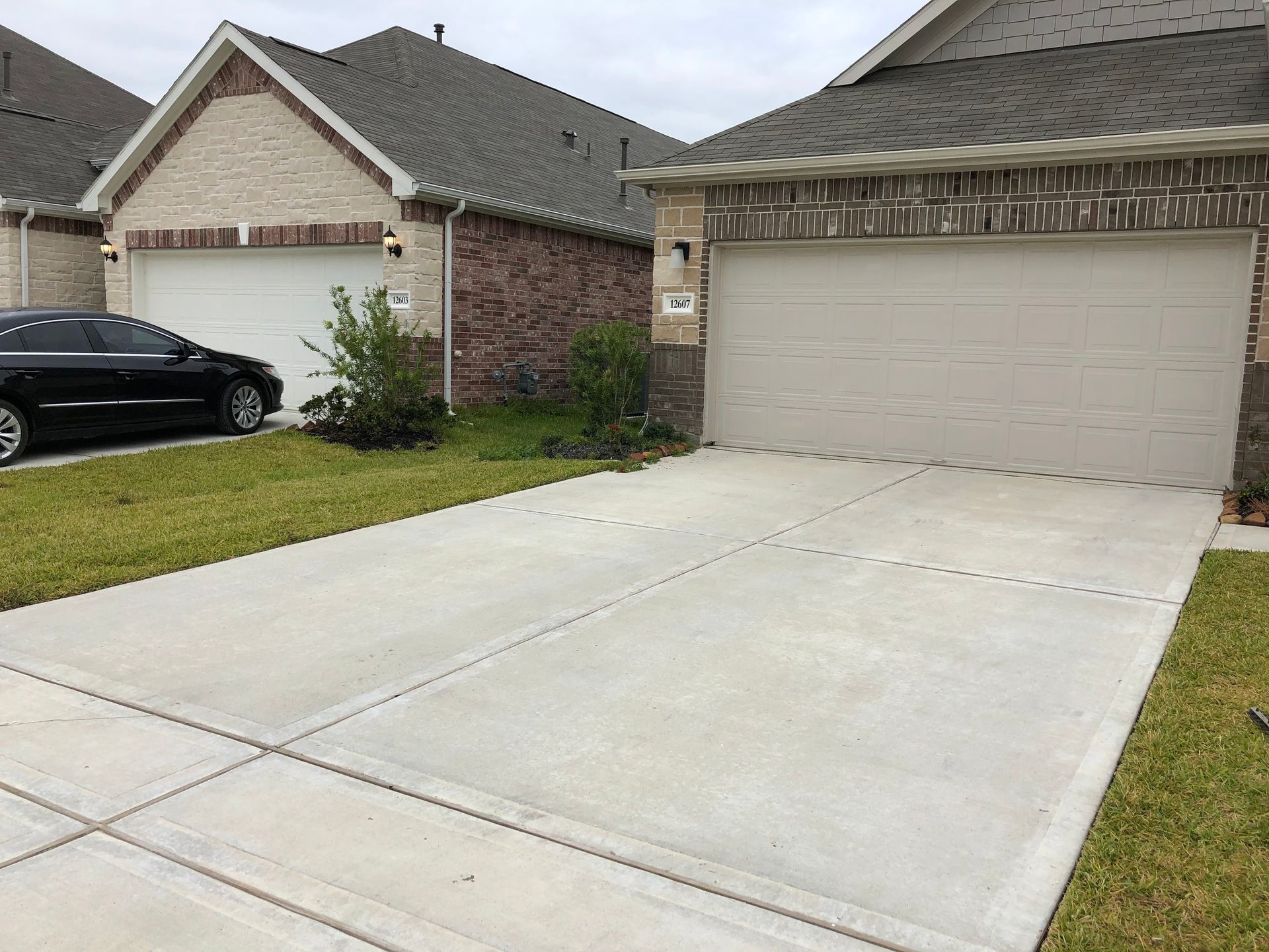 Driveway leading to two-car garage, houses with brick facades, car parked on the left.
