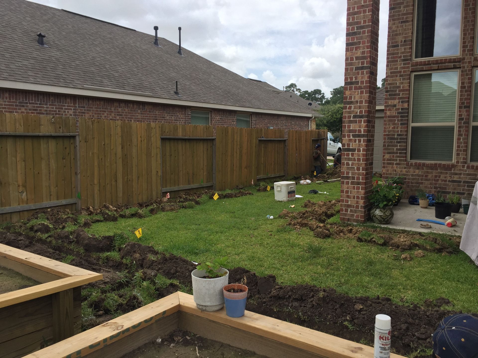 Backyard with a fence, grass, and garden beds. Construction materials scattered.