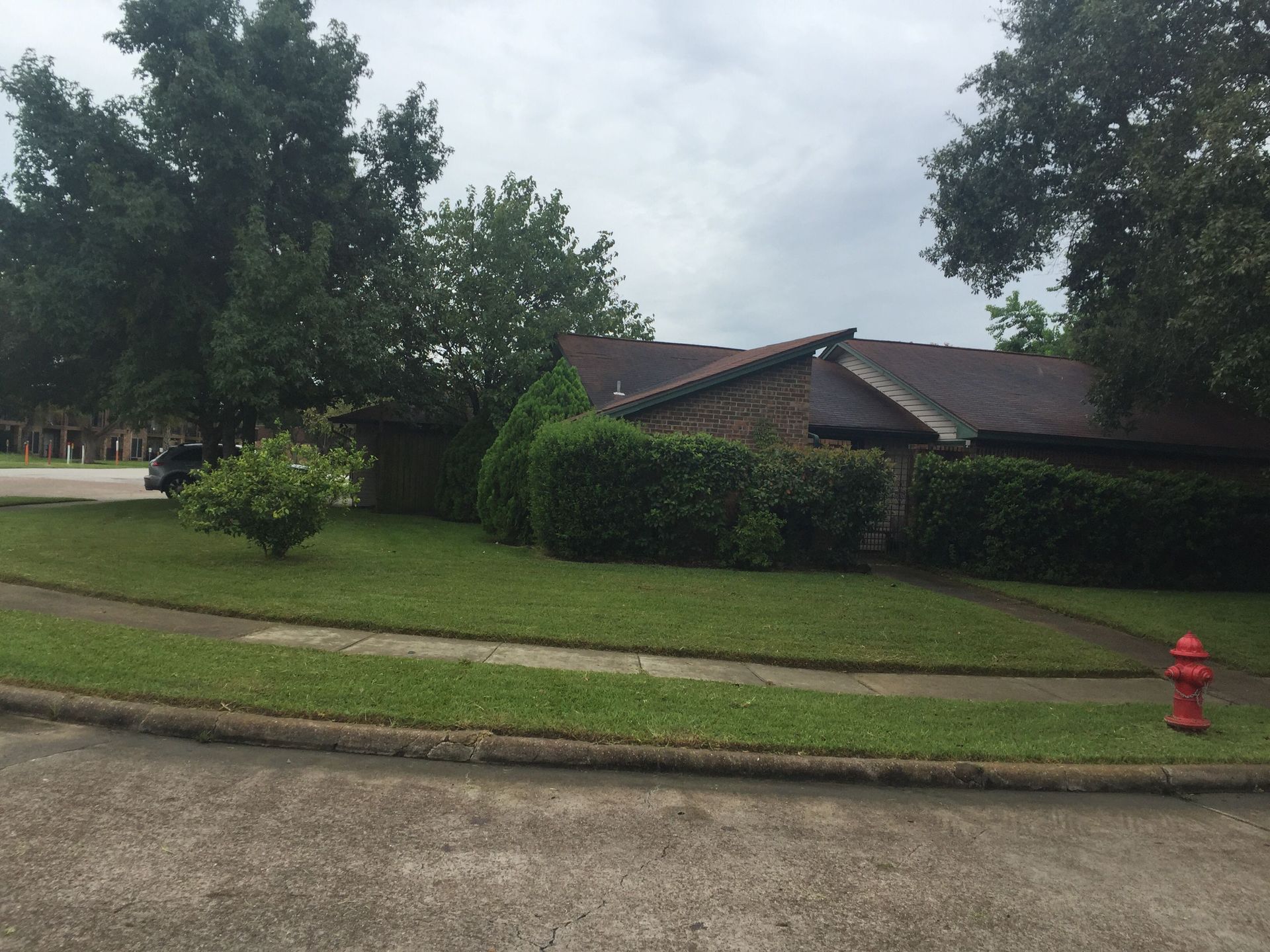 House with a brick facade, green bushes, and grass in a suburban setting with a cloudy sky.