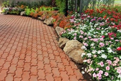 Brick path curves alongside flower bed filled with colorful blossoms.