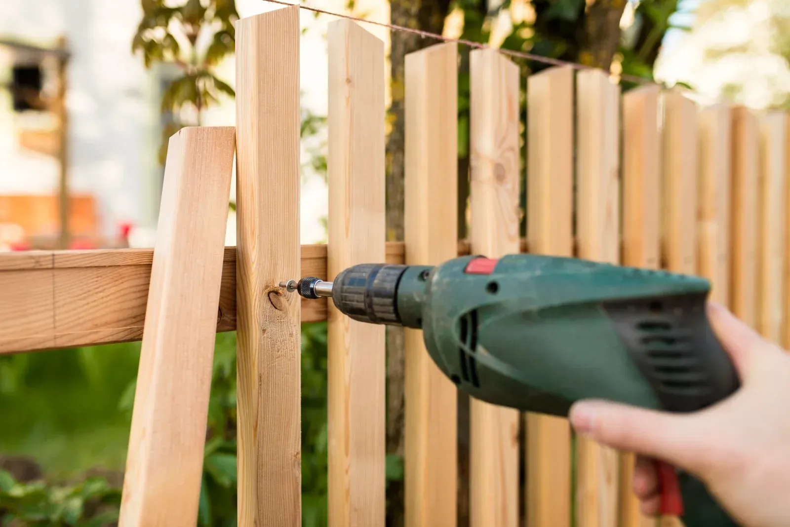 A person drills a screw into a wooden fence post.