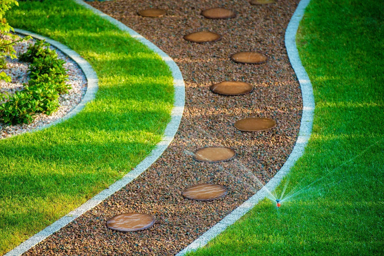 Curved pathway with stepping stones through gravel, bordered by white and green grass.