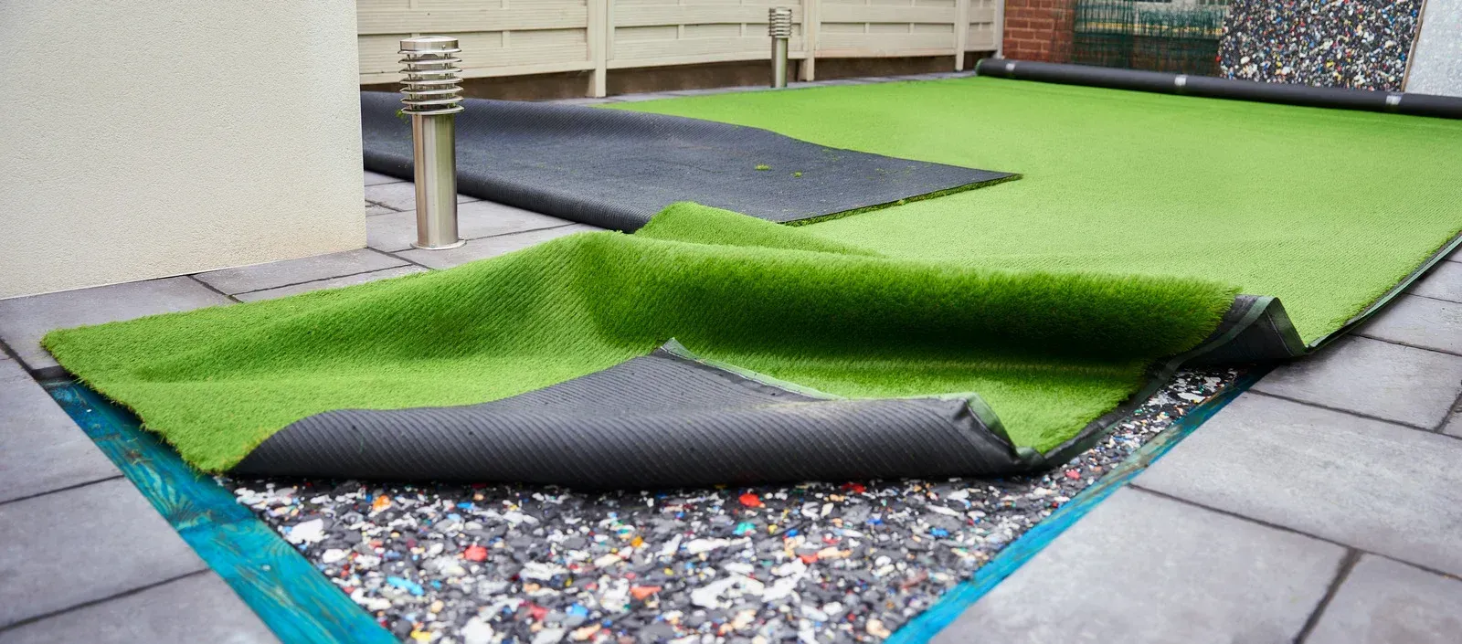 Artificial turf being installed on a patio; layers of gravel, padding, and green turf are visible.