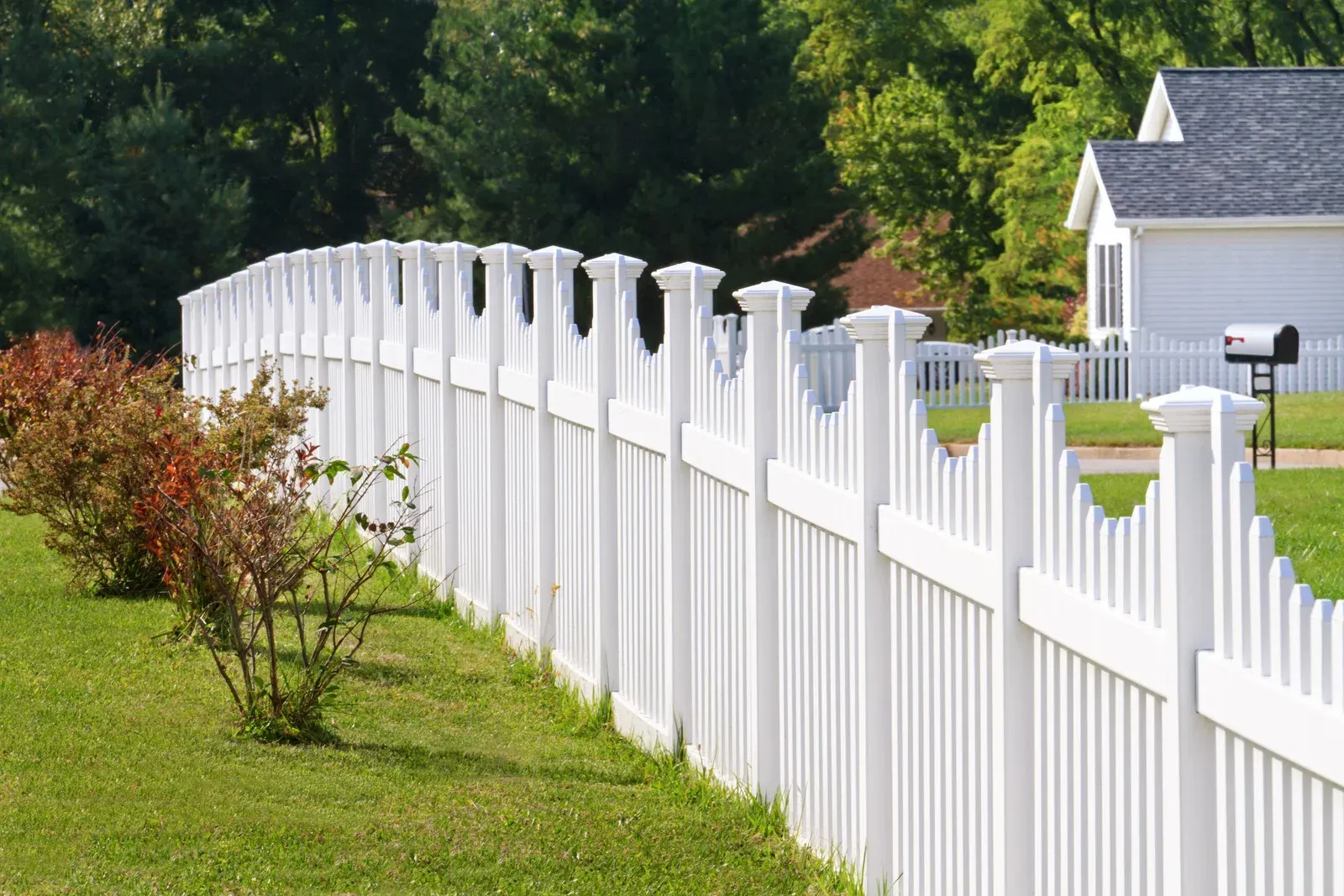 White picket fence bordering a grassy lawn in front of a house with mailbox.